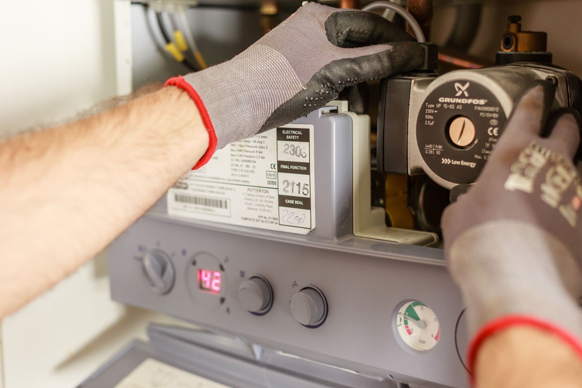 A gas engineer’s gloved hands working inside an open combi boiler, with the pump and control panel visible